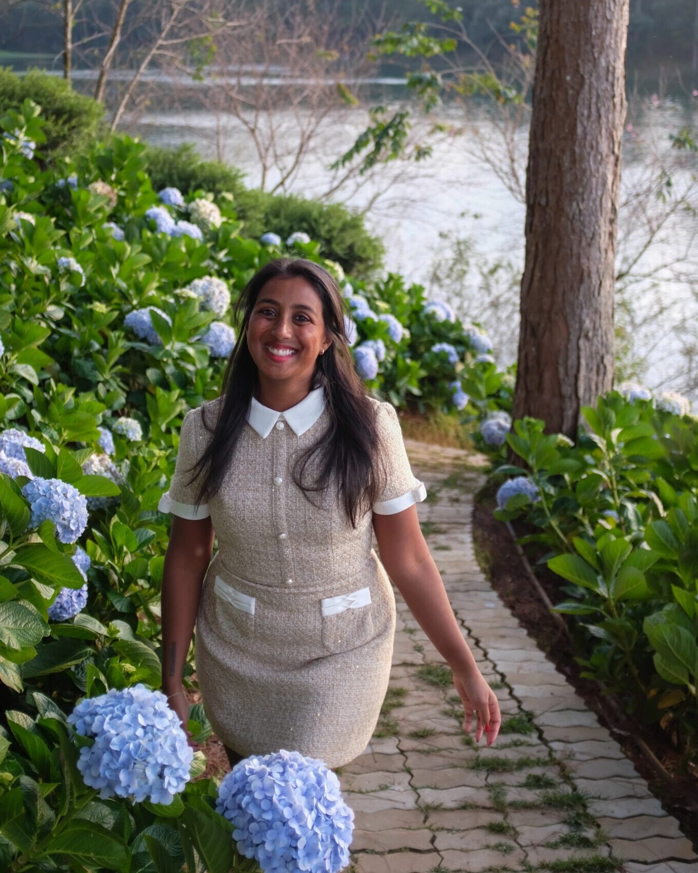 Safeena smiling on a garden path beside hydrangeas and a lake