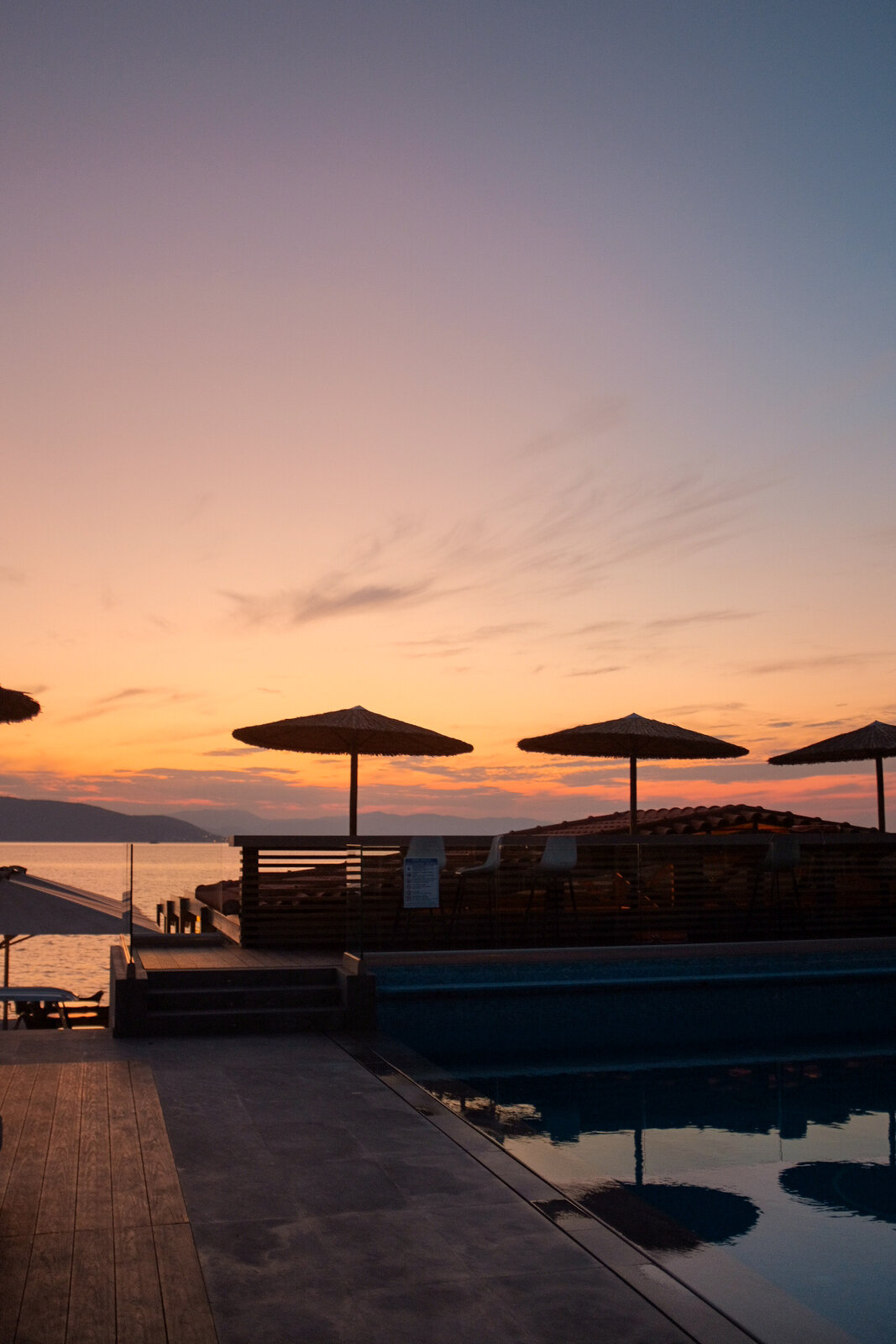 Infinity pool at sunset with straw umbrellas over the sea